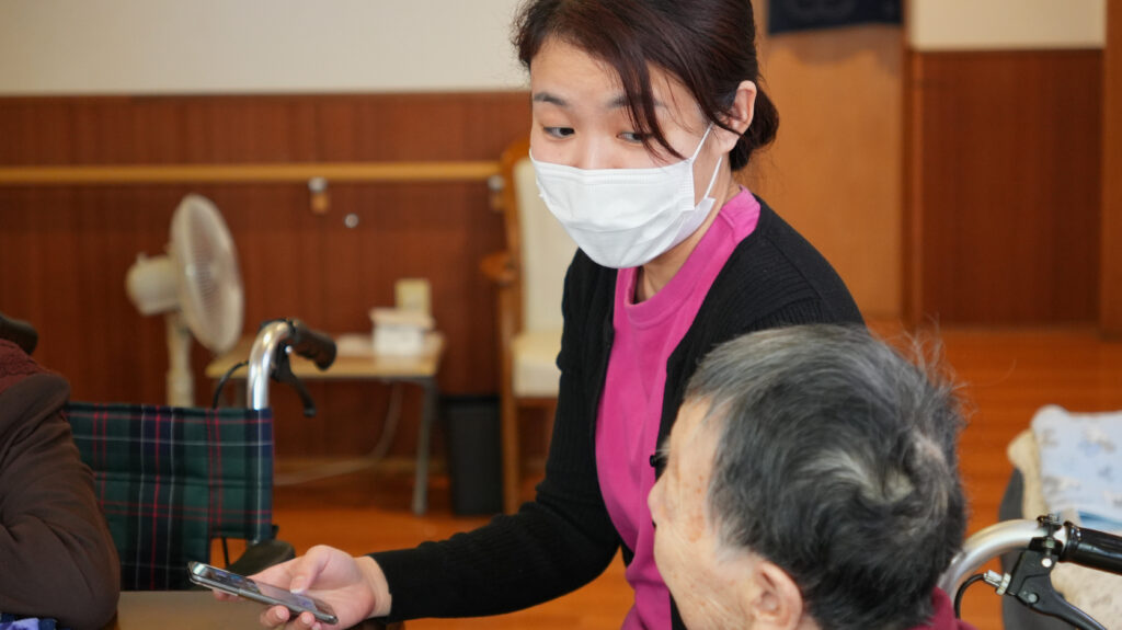 スタッフさんがご利用者の横でケアコラボを操作している写真