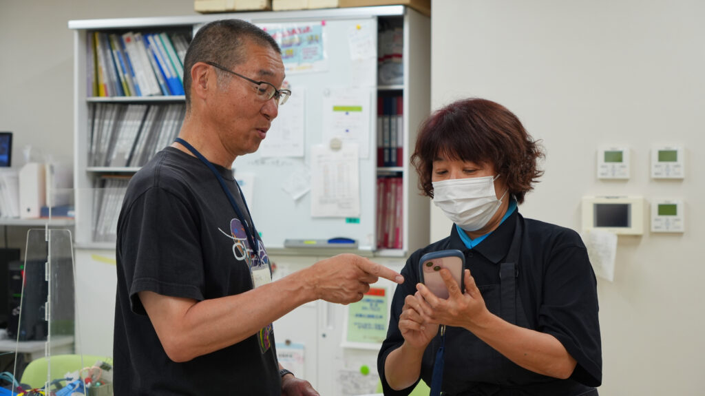 チハヤ会さまのスタッフがスマホでケアコラボを操作し、コミュニケーションを図っている様子