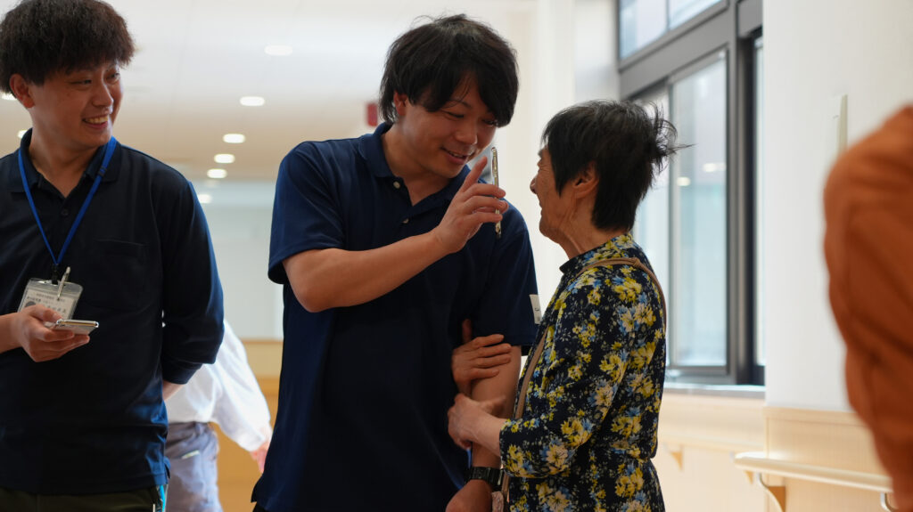 薫英会さまのスタッフが笑顔のご利用者と話し、記録を入力している様子